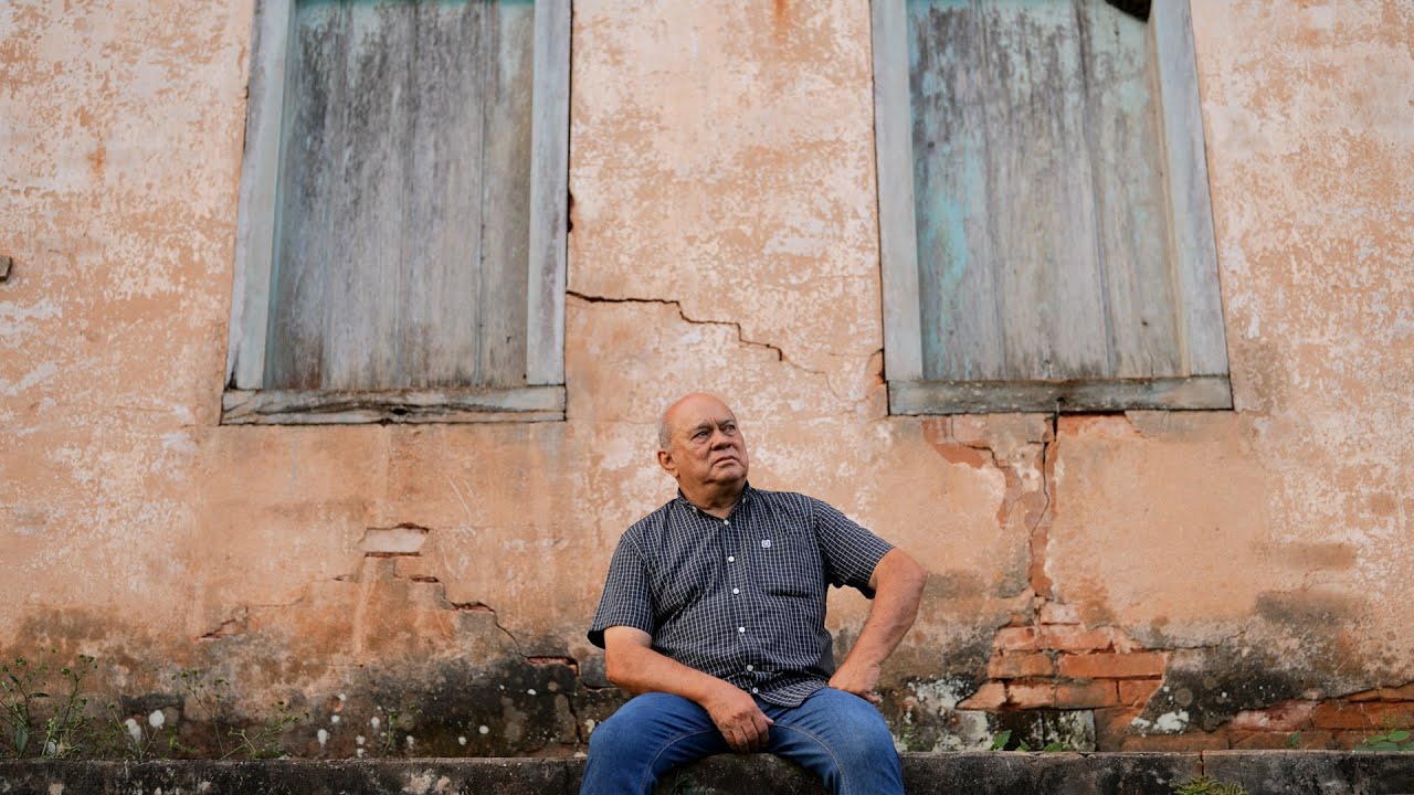 Capa do documentário de Luiz Divino, sentado diante de uma casa antiga